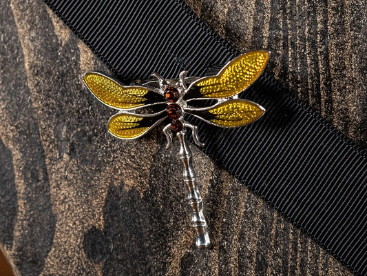 Pretty vintage dragonfly brooch with yellow and black enamel wings and and three red faux stones, set on a bright metal body.